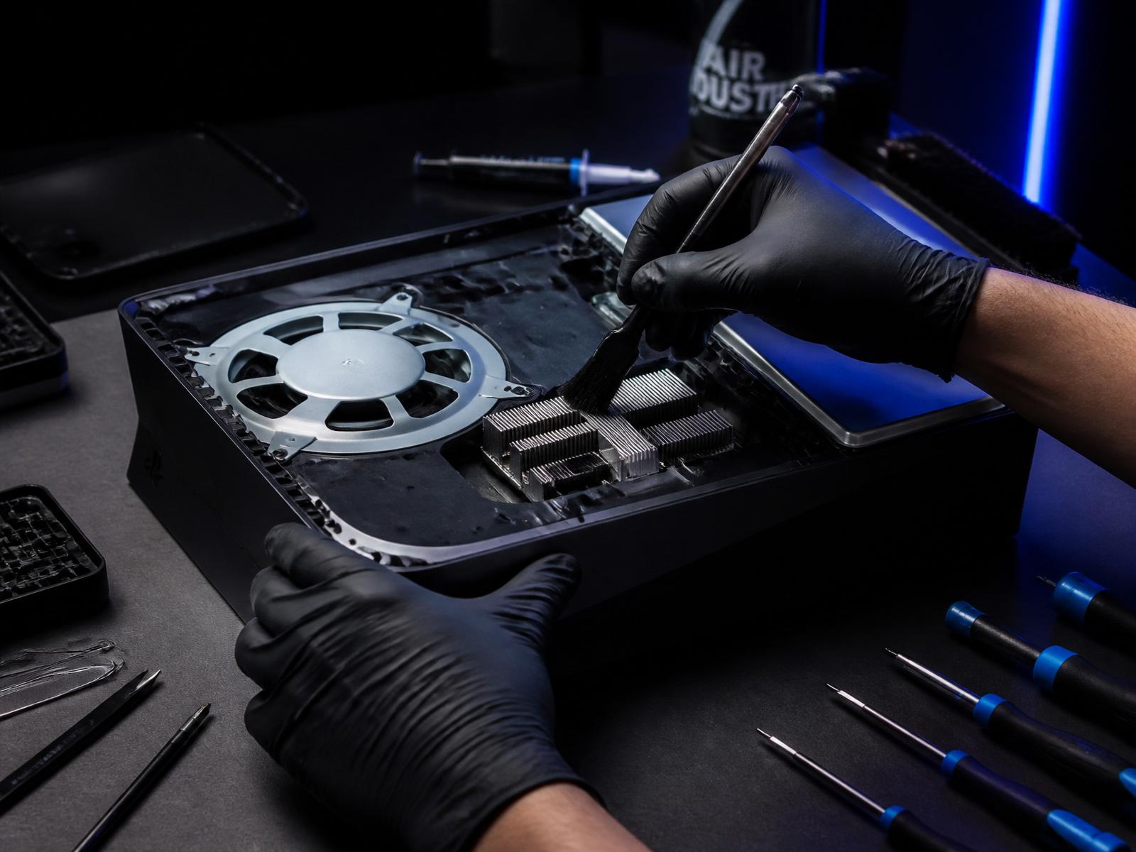 Technician carefully cleaning the fan and heatsink inside an opened game console on a workbench.
